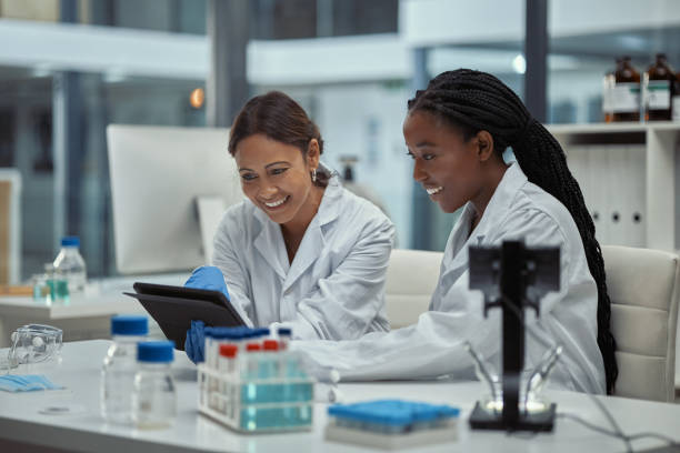 scatto di due scienziati che lavorano insieme su una tavoletta digitale in un laboratorio - teamwork medical research science women foto e immagini stock