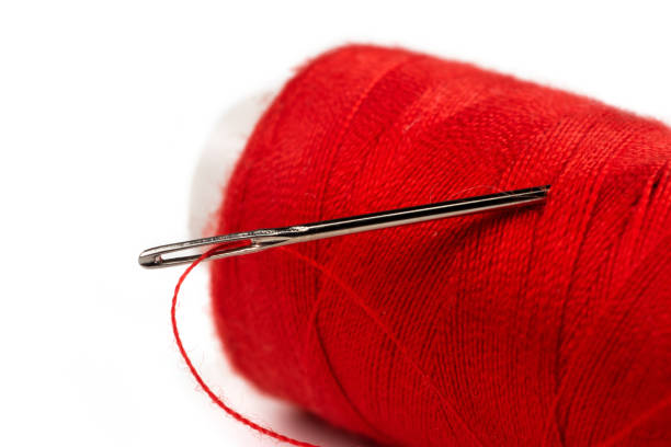 istock Eye of the needle with red polyester thread. Spool of red polyester sewing thread in the background. Selective focus. Bokeh 1370154617