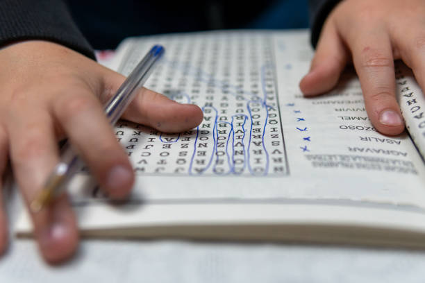 Young child entertained resolving the crossword puzzles at his grandmother's house. Pensive boy trying to solve crosswords with the pen. word game stock pictures, royalty-free photos & images