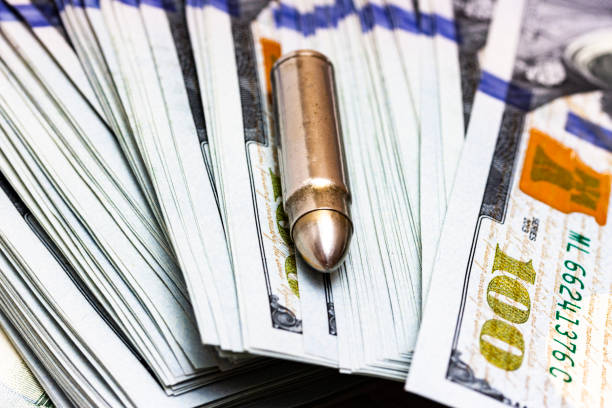 One gun bullet laying on a heap of an american one hundred dollar One gun bullet laying on a heap of an american one hundred dollar bills. Weapon and money concept. terrorist financing stock pictures, royalty-free photos & images