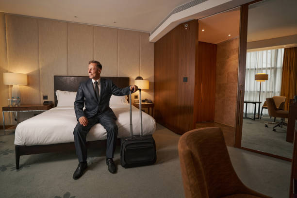 istock Enthusiastic businessman sitting on bed and checking his hotel suite 1370165843