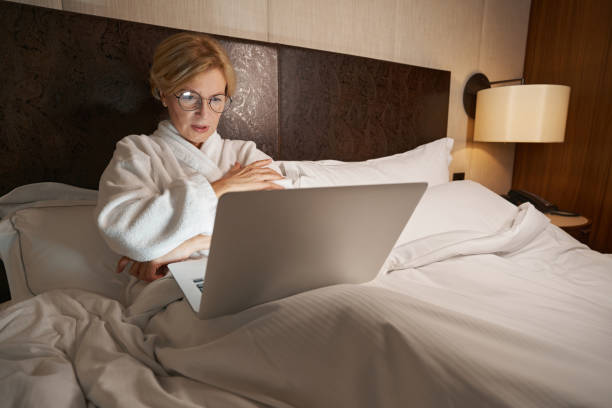 istock Concentrated lady looking at laptop while laying in cozy bed 1370166407