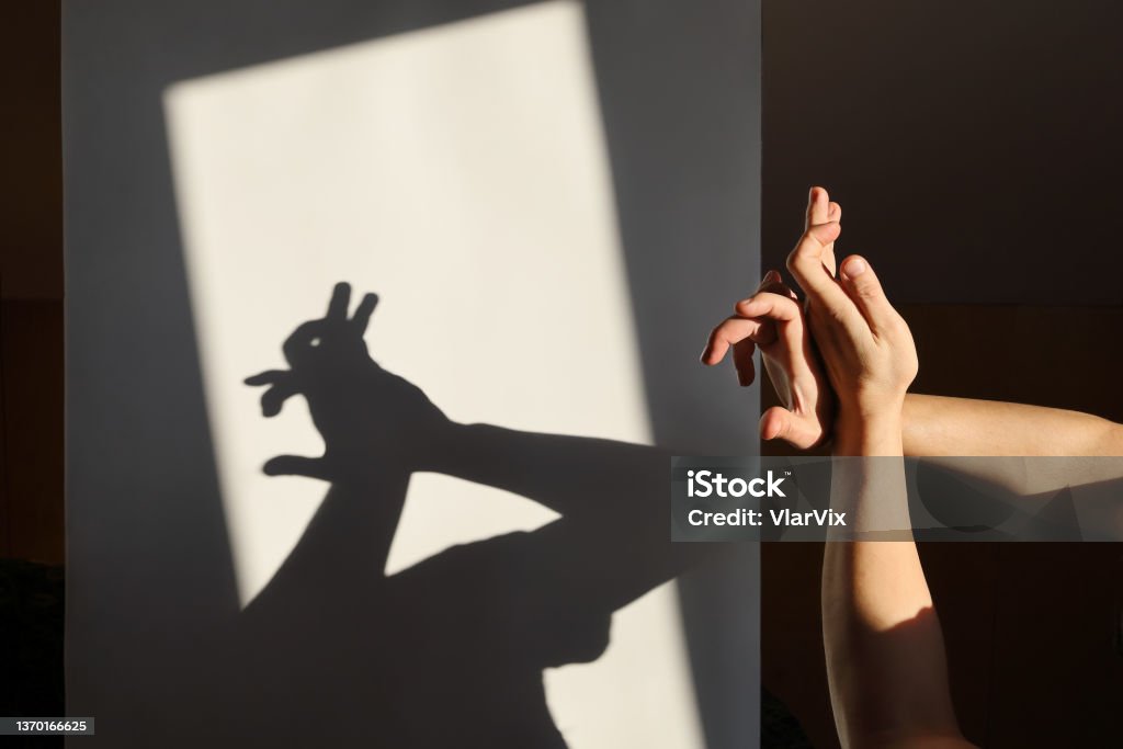 Improvised shadow theater, hands show silhouette of hare on white surface in rays of sunlight Improvised shadow theater, hands show silhouette of hare on white surface in the rays of sunlight Shadow Stock Photo