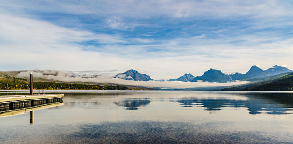 View of Lake McDonald in the morning with a jetty in the foreground, clouds in the background and a mountain range in Glacier National Park in the USA.