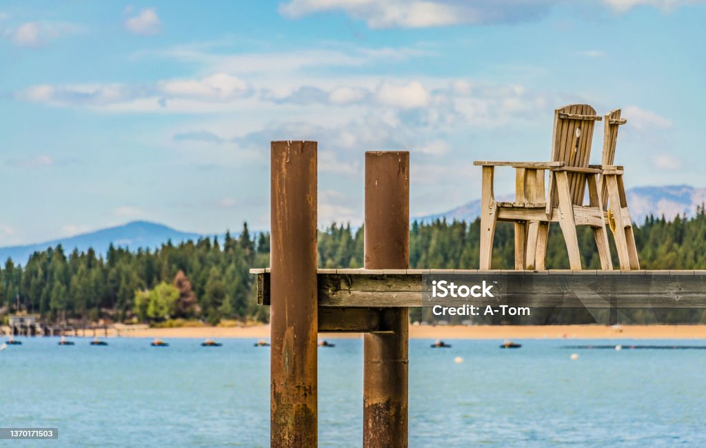 Boat dock with wooden chairs on Lake Tahoe Detailaufnahme von einem Bootssteg mit Holzstühlen mit dem Lake Tahoe, Wald und Bergen im Hintergrund South Lake Tahoe Stock Photo