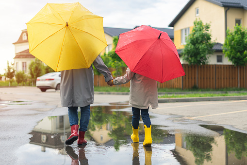 Mom and daughter rainy weather go home under umbrellas and in rubber boots. After all, with your back.