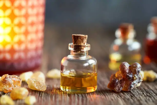 A bottle of frankincense essential oil with boswellia resin and a candle in the background