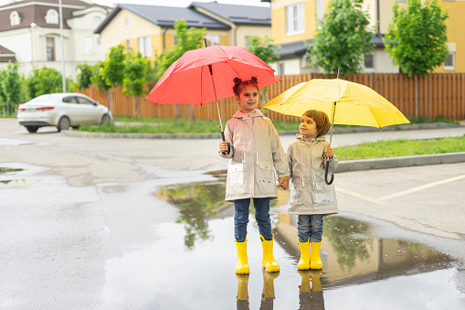 happy sister and brother in yellow rubber rain boots play with bright umbrellas in the street after the rain.