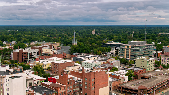Aerial shot of Durham, North Carolina on an overcast day in Fall, looking across the brick downtown buildings to the surrounding forest.