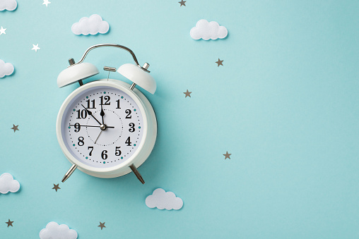 Top view photo of the white big clock and a confetti in shape of cute stars and white clouds on the isolated pastel blue background copyspace