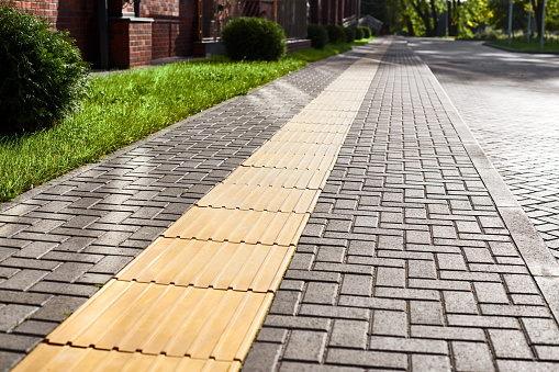 Tactile paving on pedestrian walkway, yellow tactile tiles outdoor. Tactile ground surface indicators for blind and visually impaired. Detectable warnings outside