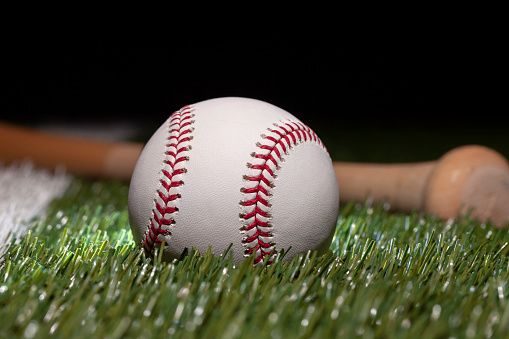 Baseball close up low angle with bat on grass field and black background