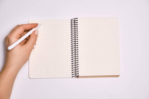 istock Woman's hand holding pen and open spiral notebook with blank white pages 1370195381