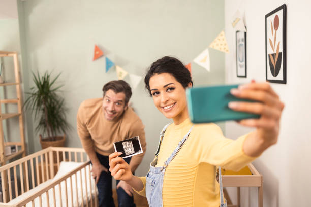 glückliches junges paar, das ein selfie mit einem ultraschallbild seines kommenden babys macht - human pregnancy telephone ultrasound family stock-fotos und bilder