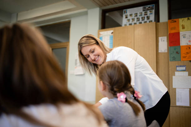 istock Smiling schoolteacher helping children with their tasks in classroom. 1370203755