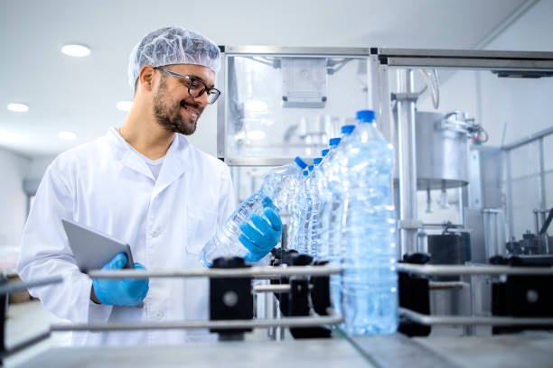 istock Industrial technologist holding tablet computer and checking production of bottled water in bottling factory on automated machine. 1370204435