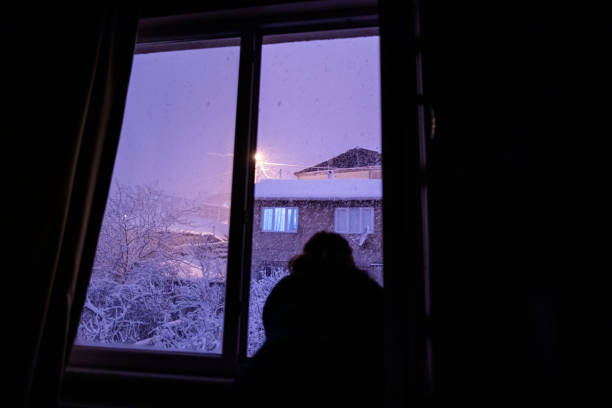 istock silhoutte of lady looking snowing from window at night time 1370205797