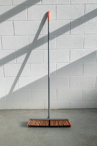Closeup of a broom against a wall in a warehouse with sunlight coming in.