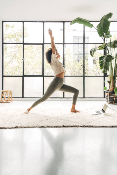 młoda afroamerykanka ćwicząca jogę w domu przy użyciu laptopa. obraz pionowy. miejsce kopiowania - living room learning healthy lifestyle one person zdjęcia i obrazy z banku zdjęć