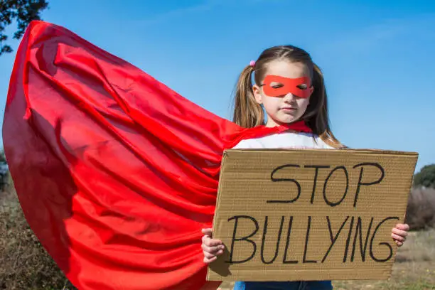 Little Girl Pretending To Be A Superheroine With A Red Mask And Red Cape, Showing A Sign That Says Stop Bullying.
