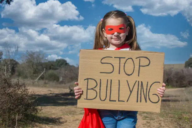Little Girl Pretending To Be A Superheroine With A Red Mask And Red Cape, Showing A Sign That Says Stop Bullying.