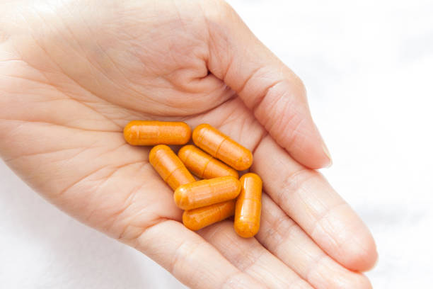Woman's hand holding orange turmeric vitamin medicine supplement pill capsules stock photo