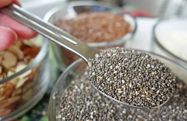 Close up view of a heaping spoon full of black chia seeds on blurred ingredient food background.