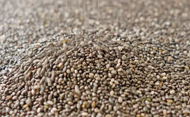 Full frame close up view of black chia seeds pouring in a heap with a blurred background.