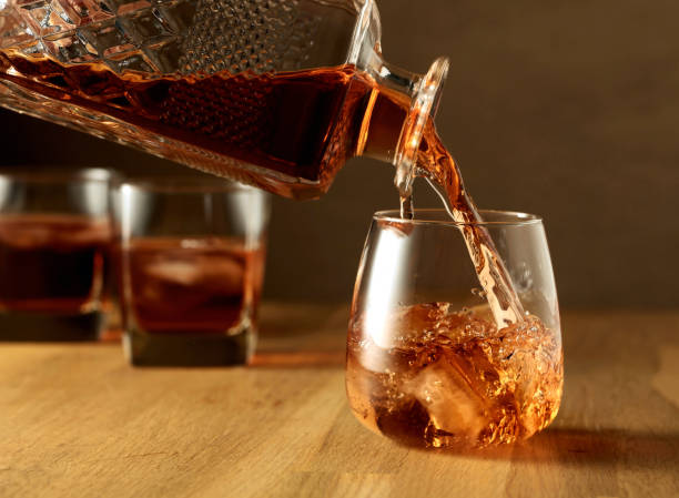 whiskey wird in ein aufgestautes glas mit eis gegossen. - wine decanter elegance pouring stock-fotos und bilder