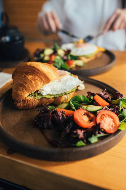 um sanduíche de croissant com ovo, tartine com abacate e ovo e um chá de ervas com bule de ferro na mesa de madeira - appetizer bread breakfast close up - fotografias e filmes do acervo