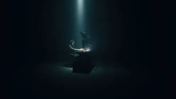 Concept shot of male hacker using computer to access private data while sitting under spotlight in darkness