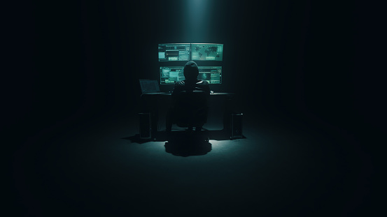 Cyberspy in an anonymous mask typing on the keyboard and attacking system data on a computer in the darkness during a cybercrime at night