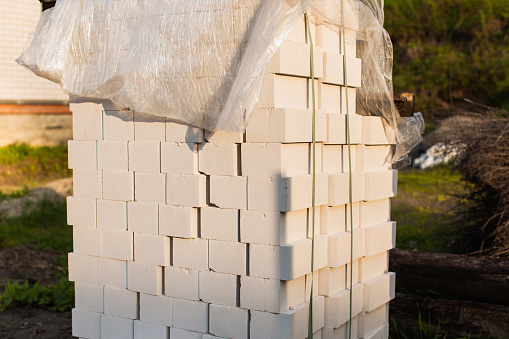 White bricks in a pile covered with cellophane. Construction of house and fence. Building materials. Construction industry