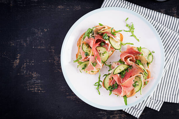 istock Breakfast or brunch.  Open sandwich with prosciutto or jamon on white plate. Mediterranean appetizer. Top view, overhead 1370268474