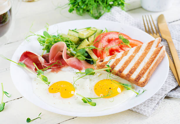 English breakfast - fried egg, jamon, toast and fresh vegetables salad. English breakfast - fried egg, jamon, toast and fresh vegetables salad. english cuisine stock pictures, royalty-free photos & images