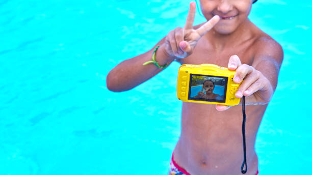 Selfie inside a pool while showing the victory symbol with his fingers. 6-year-old girl shows the victory symbol while photographing herself with an underwater camera in a swimming pool. underwater camera stock pictures, royalty-free photos & images