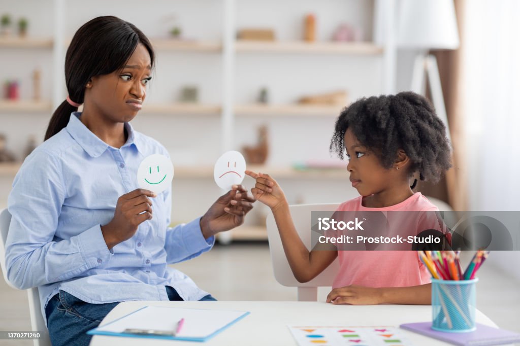 Female psychologist and little black girl exercising at daycare Female psychologist friendly pretty young black woman and little girl preschooler exercising at daycare, learning about emotions, copy space. Child development, emotional intelligence for kids concept Child Stock Photo