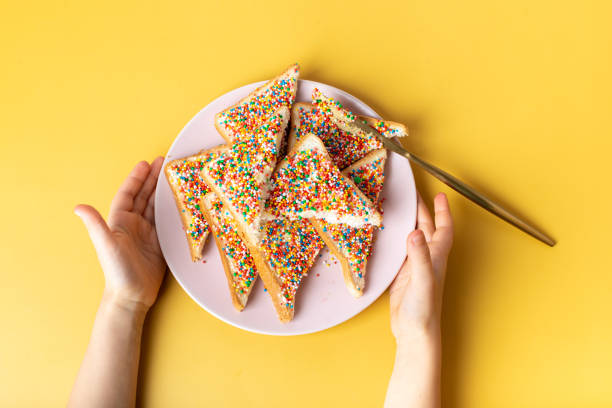 pan de hadas en mano. la famosa comida tradicional australiana fairy bread sobre un fondo amarillo - downunder fotografías e imágenes de stock