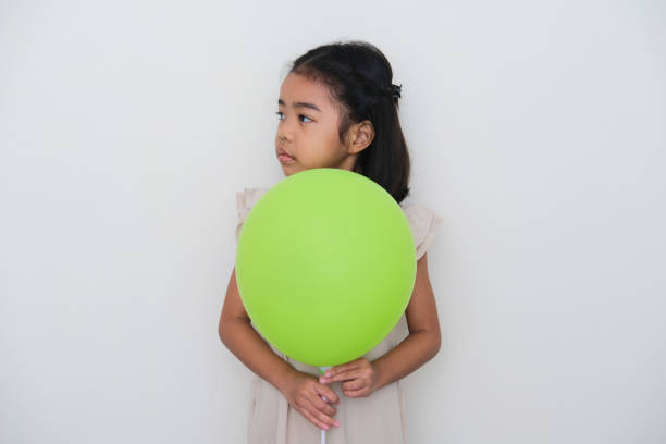 Asian kid looking to the right side with sad expression while holding green balloon Asian kid looking to the right side with sad expression while holding green balloon keluarga stock pictures, royalty-free photos & images