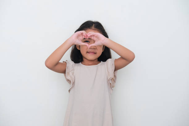 Asian kid smiling while peeking from heart shaped hand. Love concept Asian kid smiling while peeking from heart shaped hand. Love concept keluarga stock pictures, royalty-free photos & images