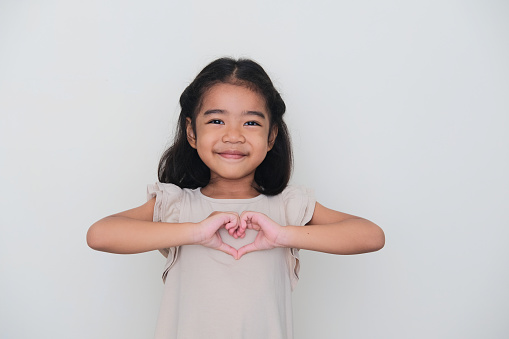 Asian kid smiling with her hand making heart shape on chest