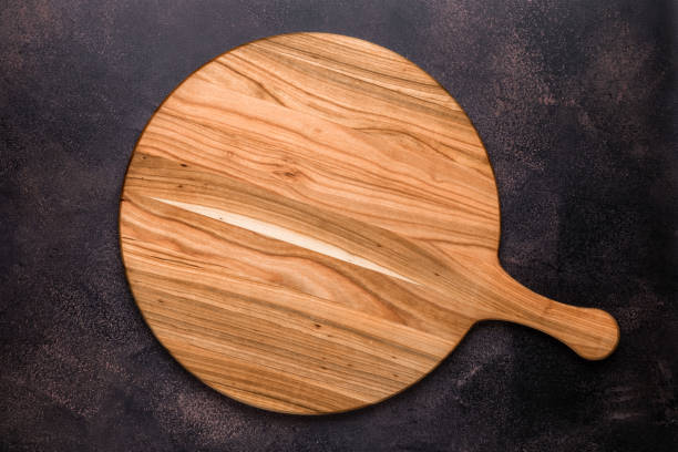 Round empty wooden charcuterie serving board with handle on old dark brown shabby table. View from above. Top view. Food background. Template with copy space for text. Flat lay, mockup. Layout, frame tabla redonda vacía de charcutería de madera con asa en una vieja mesa en mal estado de color marrón oscuro. vista desde arriba. vista superior. fondo alimentario. plantilla con espacio de copia para texto. tendido plano, maqueta. maquetación, marco.