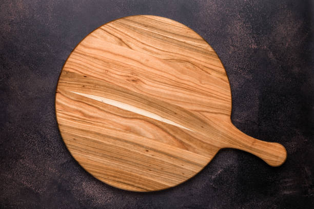 Round empty wooden charcuterie serving board with handle on old dark brown shabby table. View from above. Top view. Food background. Template with copy space for text. Flat lay, mockup. Layout, frame. stock photo