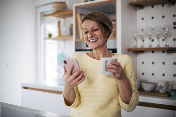 Senior woman in kitchen drink coffee and using phone. stock photo