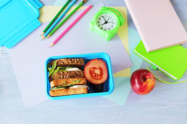 istock Lunchbox with cereal bread sandwich with cheese, organic vegetables and micro greens, apple, stationery and alarm clock 1370296765
