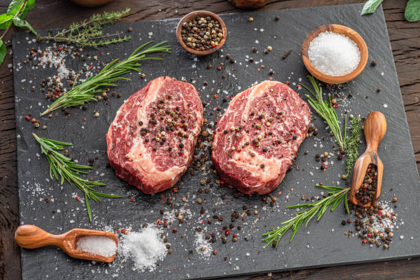 istock Raw Ribeye steaks with salt and herbs on grey board. Top view. 1370296781