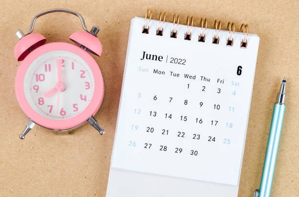 istock Junel 2022 Desk calendar with pink alarm clock on brown background. 1370297712