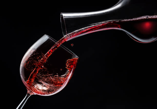 istock Red wine is poured into a wine glass on a black background. 1370298744