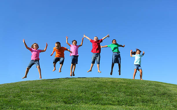 gruppo multi-etnico bambini saltare insieme - hill grass park sky foto e immagini stock