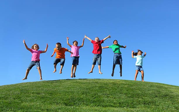 group of multi-ethnic детей прыжки вместе - hill grass park sky стоковые фото и изображения